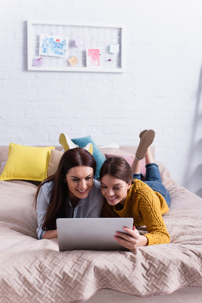 vrolijk moeder en tiener meisje kijken film op laptop in slaapkamer - Foto, afbeelding