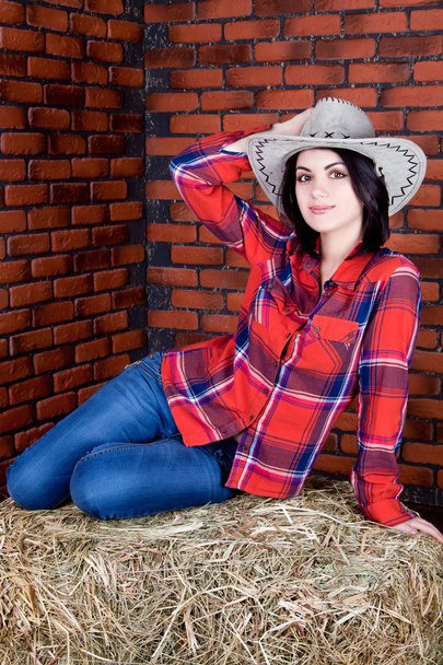 Tyttö cowboy istuu heinää ja pitää hattunsa päätään
 - Valokuva, kuva
