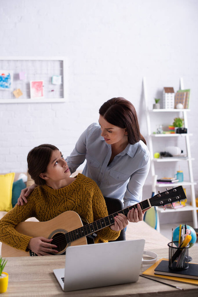 madre e adolescente che suonano la chitarra acustica vicino al laptop  - Foto, immagini