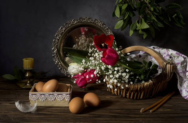 La composición de Pascua. Los huevos, los tulipanes rojos, la vela en el candelero y las velas de iglesia sobre la mesa de madera el primer plano. - Foto, Imagen