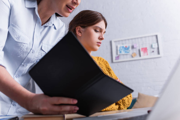 мать держит ноутбук около расстроенной дочери-подростка - Фото, изображение