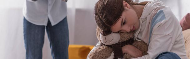 sconvolto adolescente abbracciare orsacchiotto vicino alla madre su sfondo sfocato, banner - Foto, immagini