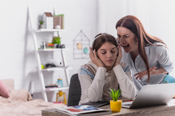 mother screaming at teenage girl in wireless headphones sitting at desk - Photo, Image