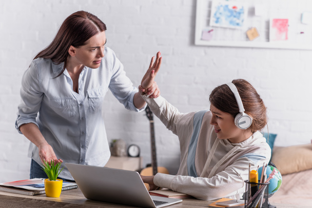 teenage girl in wireless headphones gesturing while quarrelling with mother  - Photo, Image