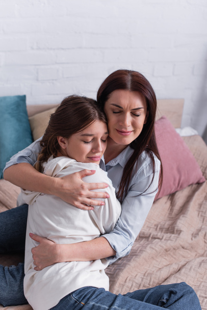 madre cariñosa abrazando hija adolescente en el dormitorio  - Foto, Imagen