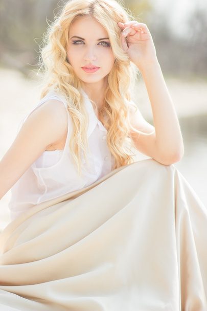 Portrait of a beautiful young blonde woman with wavy hair in nature - Фото, изображение