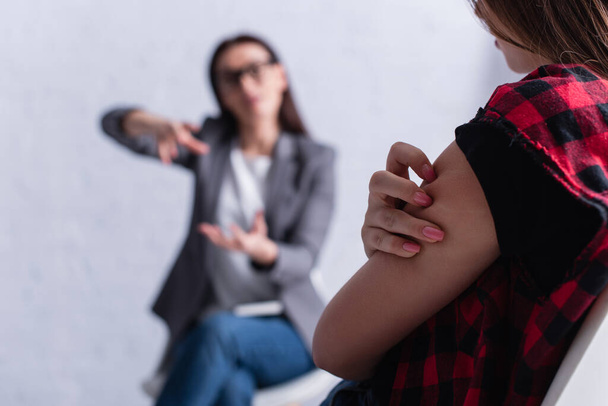 teenage patient scratching skin near psychologist on blurred foreground  - Photo, Image