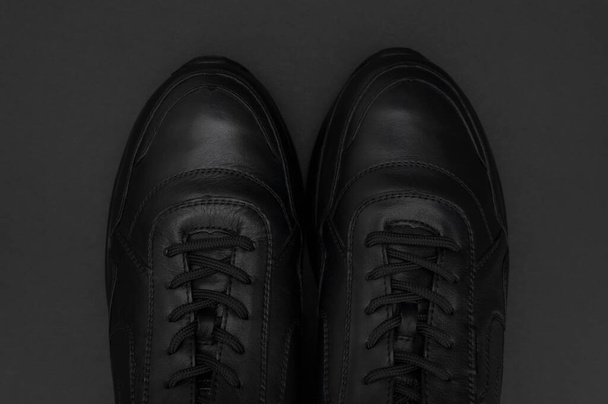 Flat lay Zwarte klassieke lederen heren sneakers op zwarte achtergrond. Modieuze jeugdsportschoenen. Sport casual schoenen bovenaanzicht kopieerruimte. Schoeisel voor fitness, hardlopen, gezonde levensstijl. - Foto, afbeelding