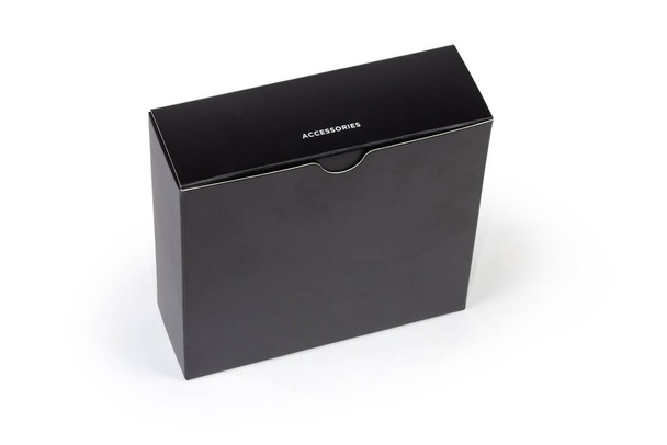Caja de embalaje de cartón plano rectangular negro cerrado de accesorios con pie de inscripción correspondiente sobre un fondo blanco - Foto, imagen