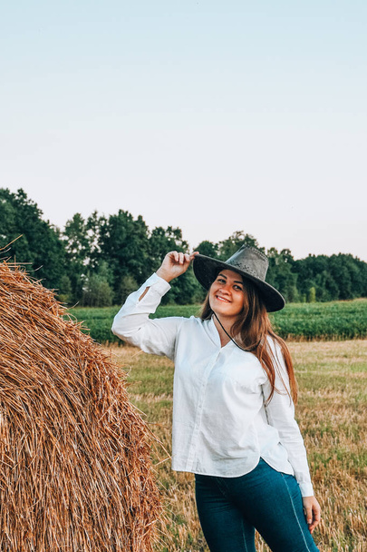 Kobieta w kowbojskim kapeluszu zatrzymała się w pobliżu słomki. Lato, piękno, moda, urok, koncepcja stylu życia. Rdzeń rolniczy Cottagecore - Zdjęcie, obraz