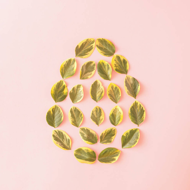 Zielone żółte liście ułożone w kształcie jajka na różowym tle. Koncepcja wielkanocna 2021. Płaskie lay minimalny styl. - Zdjęcie, obraz