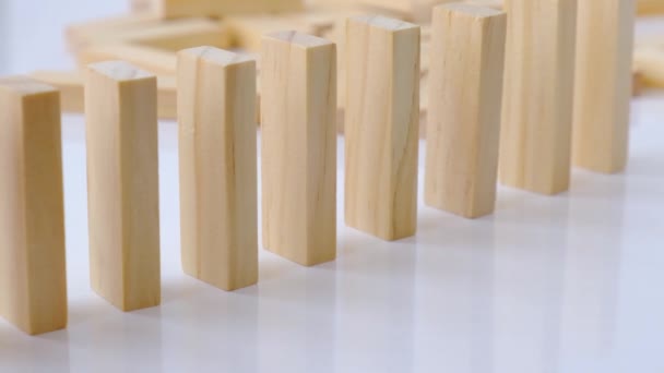 Dominoeffekt, eine Reihe von hölzernen Dominosteinen, die auf weißem Hintergrund herunterfallen. Dominosteine fallen hintereinander, die Hand schiebt einen Domino und löst eine Kettenreaktion aus Brettspiel. - Filmmaterial, Video