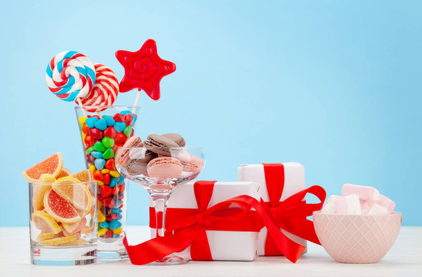 Diverse zoetigheden assortiment. Snoep, bonbon, chocolade en macarons in cocktailglazen en geschenkdozen op blauwe achtergrond. met kopieerruimte - Foto, afbeelding