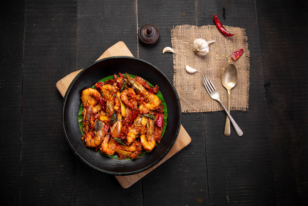  Kerala style Prawns roast or chemmeen varattiyathu  made using red kashmiri chilli flakes and coconut slices as main ingrediants and garnished with onion rings and tomato slices ,placed on a black textured background. - Photo, Image