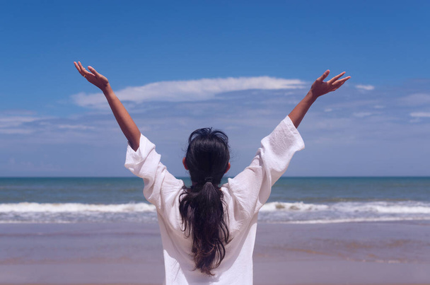 people and healthy lifestyle concept - back view young woman enjoying tropical sea view with arms up feeling free bliss with blue sky background - Photo, Image