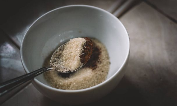 Medição de açúcar e pó de café instantâneo por colher de sopa em uma tigela branca. preparação de ingredientes para fazer espuma de café Dalgona. uma colher de açúcar e mistura de café vista de perto. - Foto, Imagem