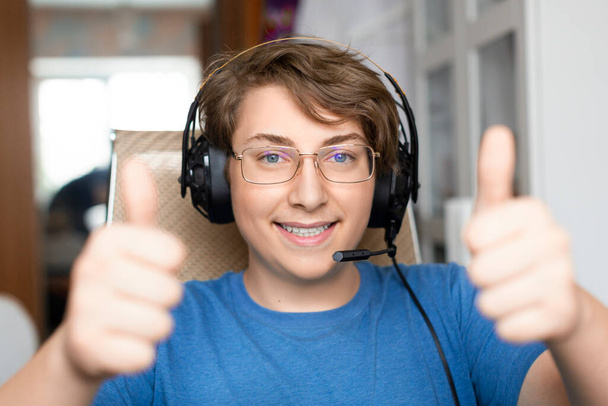 Sonriente adolescente chico mantiene pulgares hacia arriba diring videollamada en línea. - Foto, imagen
