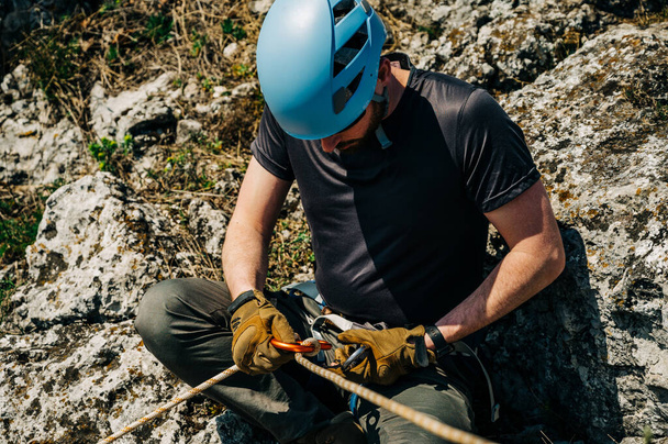 Close up of a man in harness with rock climbing equipment getting ready to rappelling outdoor. He is preparing rope in figure eight for rappelling. Climber with gear and equipment on the belt.  - Foto, imagen