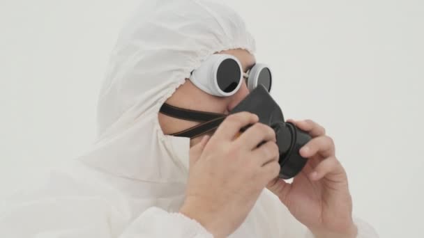 lähikuva miehestä valkoisessa kemiallisessa suojapuvussa laittamassa kaasunaamaria päälleen. Kuvattu valkoisella taustalla. - Materiaali, video