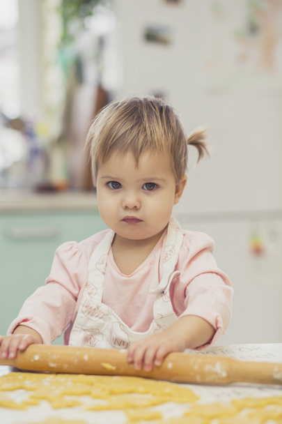 Чарівна дитина в фартусі розкачує тісто на кухні
 - Фото, зображення