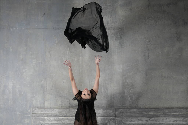 Tänzerin in Bewegung wirft sich einen Schal aus durchscheinendem schwarzen Material über den Kopf - Foto, Bild