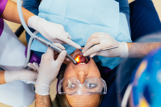 Immagine dall'alto di un dentista che cura i denti di un paziente insieme al suo assistente. Le mani del dentista che lavorano sulla cura dei denti. - Foto, immagini
