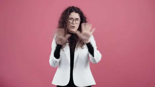 Exhausted young woman with curly hair, shows the stop sign with her palms, looking into the room. Young hipster in white jacket and black shirt, with glasses posing isolated on pink background in the - Footage, Video
