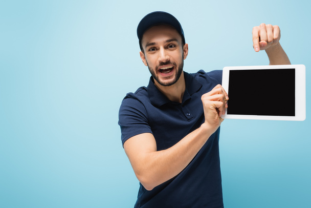 κατάπληκτος arabian delivery man δείχνοντας σε ψηφιακή ταμπλέτα με λευκή οθόνη που απομονώνονται σε μπλε - Φωτογραφία, εικόνα
