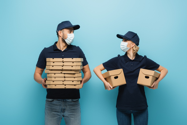 multicultural couriers in medical masks looking at each other on blue - Photo, Image