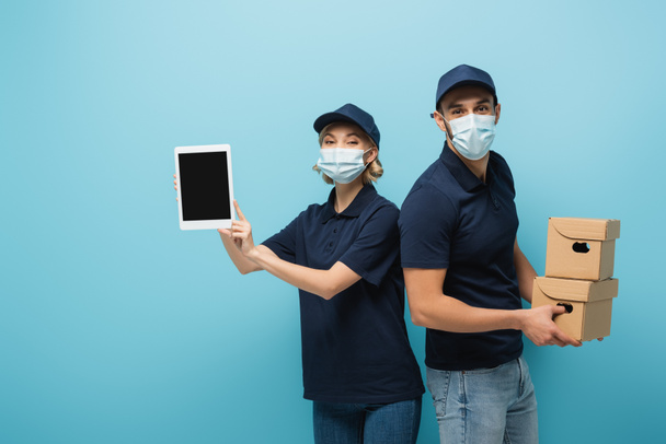 mensageiros inter-raciais em máscaras médicas, com tablet digital e caixas de papelão isoladas em azul - Foto, Imagem