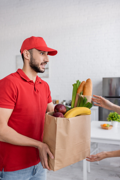 woman taking paper bag with fresh food from young muslim delivery man - Photo, Image
