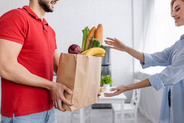 consegna uomo in possesso di cibo fresco in sacchetto di carta vicino donna sorridente - Foto, immagini