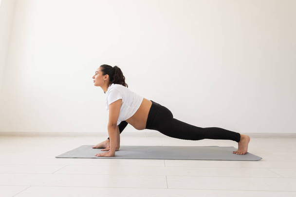 Joven mujer embarazada flexible haciendo gimnasia en la alfombra en el suelo sobre fondo blanco. El concepto de preparar el cuerpo para el parto fácil - Foto, Imagen