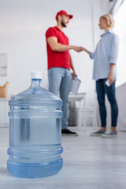 selective focus of big bottle of potable water near muslim courier and woman shaking hands on blurred background - Photo, Image