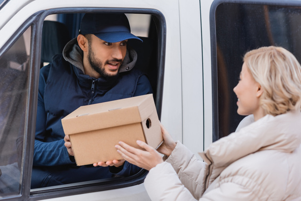 muslim postman in truck giving parcel to blonde woman on blurred foreground - Photo, Image