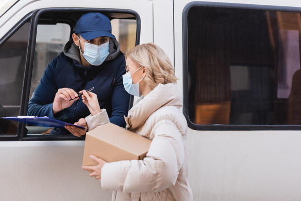 muslim courier in medical mask giving pen to woman holding parcel - Photo, Image