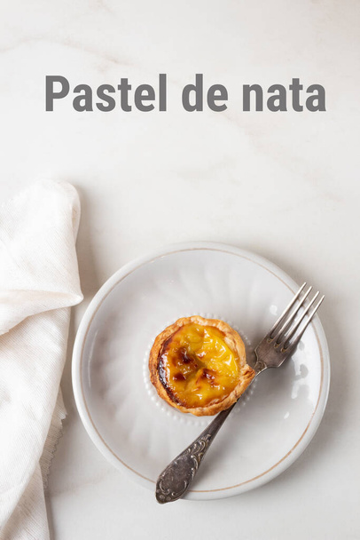 パステル・デ・ナタ(Pastel de Nata) -白い大理石の背景にあるポルトガルの卵のカスタードパイ。フォークでセラミックプレート上のポルトガルのパティ,トップビュー - 写真・画像