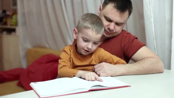 Iskoláskorú gyerek és az apja együtt olvas egy könyvet otthon, Apák napja, tanulás és oktatás - Felvétel, videó