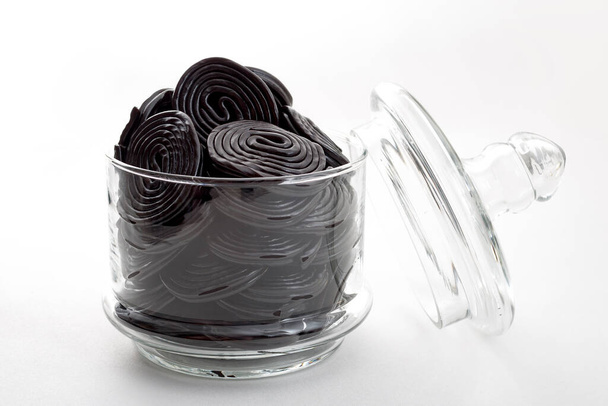 Espirales de regaliz negro, caramelos masticables y delicioso concepto de postre con ruedas de regaliz que se aromatizan con el extracto de la raíz de la planta glabra Glycyrrhiza, en un frasco de vidrio transparente - Foto, Imagen