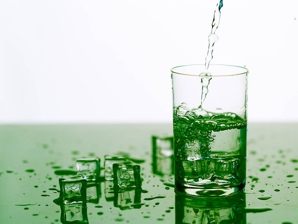 брызги чистой воды в стакане со льдом, прозрачная вода в стакане с брызгами крупным планом - Фото, изображение