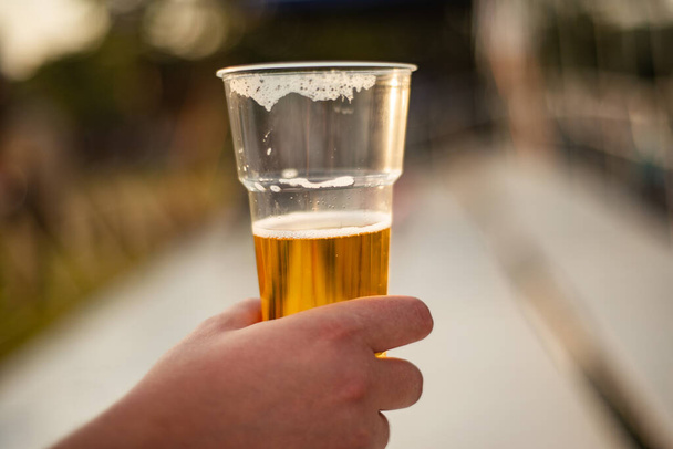 cerveza en un vaso de plástico en mano - Foto, Imagen