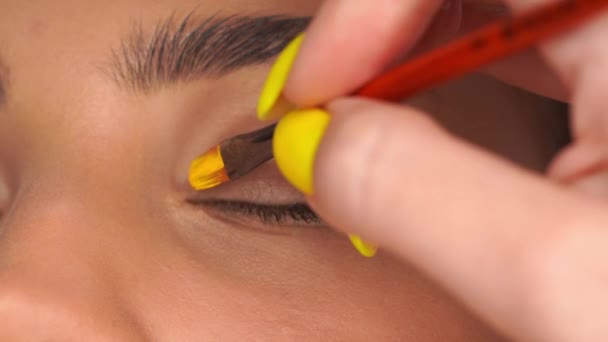 vista cortada da mulher aplicando sombra olho cremoso amarelo com escova cosmética - Filmagem, Vídeo