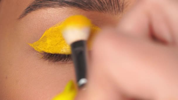 abgeschnittene Ansicht einer Frau mit geschlossenen Augen, die einen leuchtend gelben Lidschatten aufträgt - Filmmaterial, Video