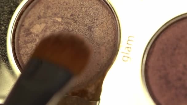 primer plano de cepillo cosmético cerca de sombra de ojos marrón con letras glam - Imágenes, Vídeo