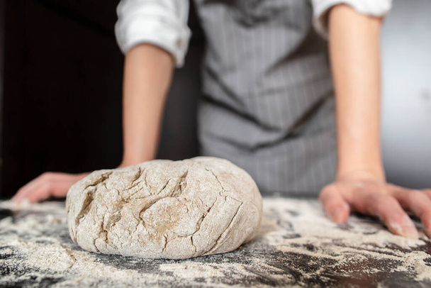準備された生地は、パン屋の手の背景に、小麦粉を振りかけたテーブルの上にあります。パン作り.  - 写真・画像