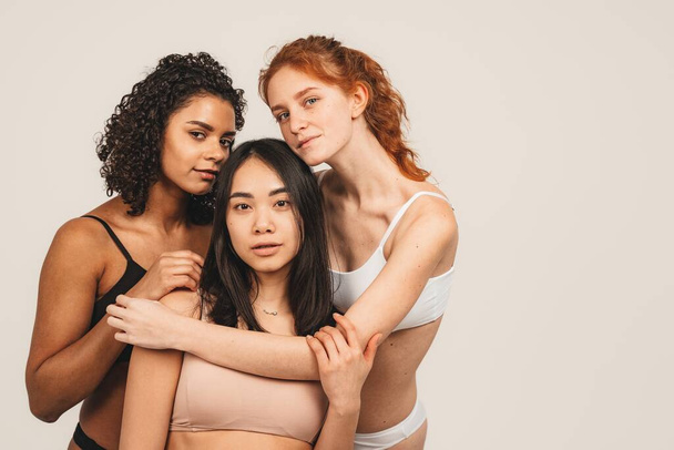 Photo of optimistic young women, multiracial friends wear underwear, hug each other and show their love. Concept natural beauty and girl power - Photo, Image