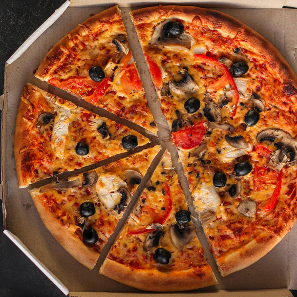 pizza met peperoni, tomaten, kaas, champignons en olijven op een zwarte achtergrond. bovenaanzicht. - Foto, afbeelding