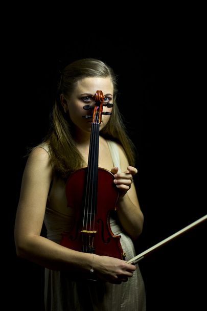Красива блакитноока дівчина грає на червоній скрипці в темряві
 - Фото, зображення