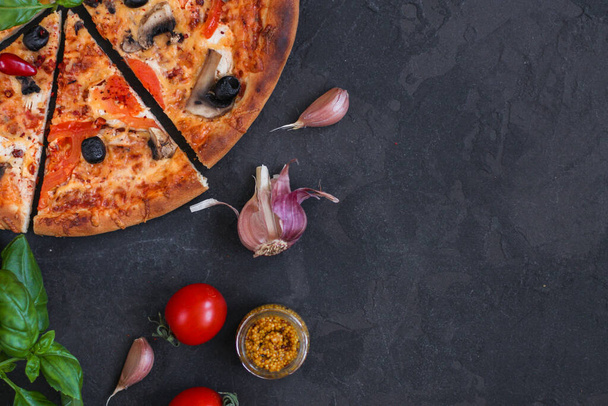 pizza con pepperoni, tomates, queso, champiñones y aceitunas sobre un fondo negro. vista superior. - Foto, imagen