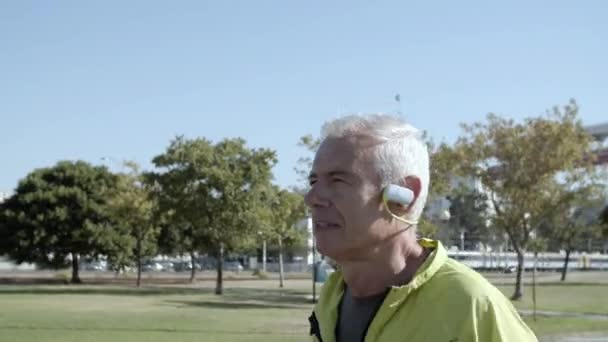 Vieja corredora activa con auriculares corriendo fuera - Imágenes, Vídeo